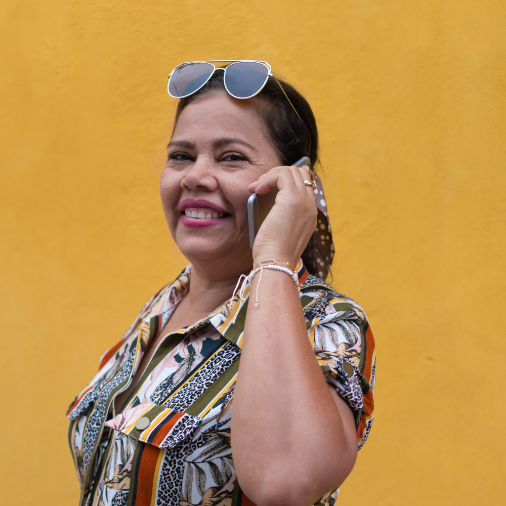 Mujer sonriente hablando por teléfono fondo amarillo.